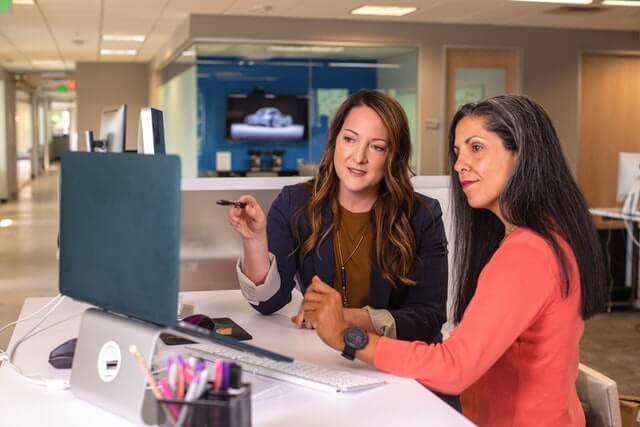 A woman consulting another women in front of a computer.