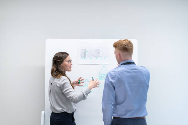 A woman presenting her presentation in a white board in front of a male colleague.